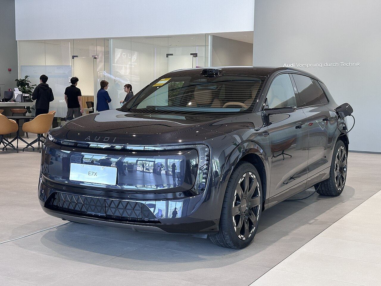 Ciemny AUDI E7X, duży elektryczny SUV z napisem AUDI na przedzie, widok z przedniego narożnika
