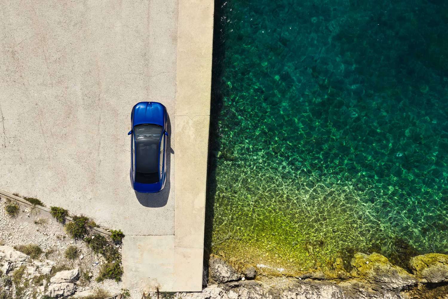 Niebieskie BMW i3 50 xDrive na betonowym pomoście nad morzem, widok z góry