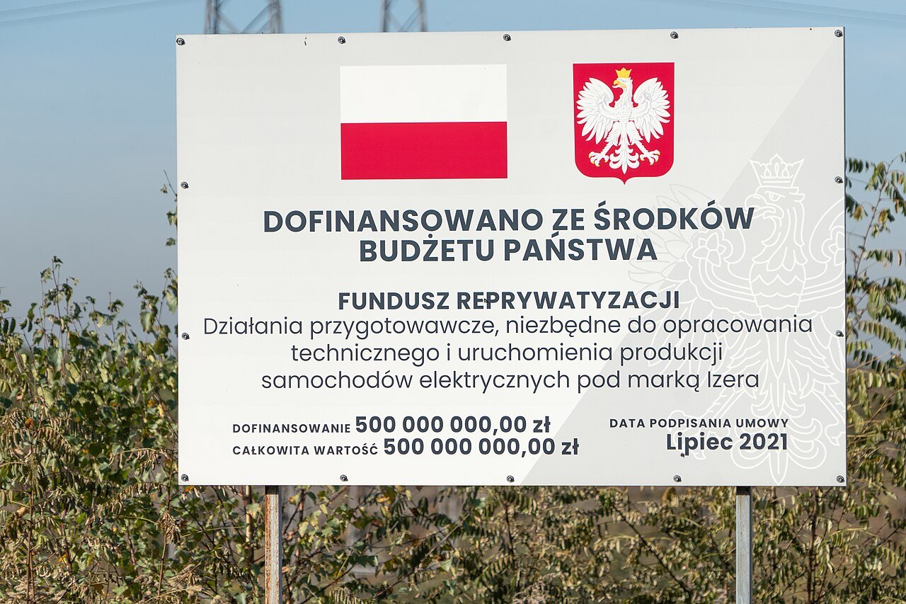 Tablica informacyjna o dofinansowaniu prac przygotowawczych do produkcji samochodów elektrycznych na terenie inwestycji w Jaworznie