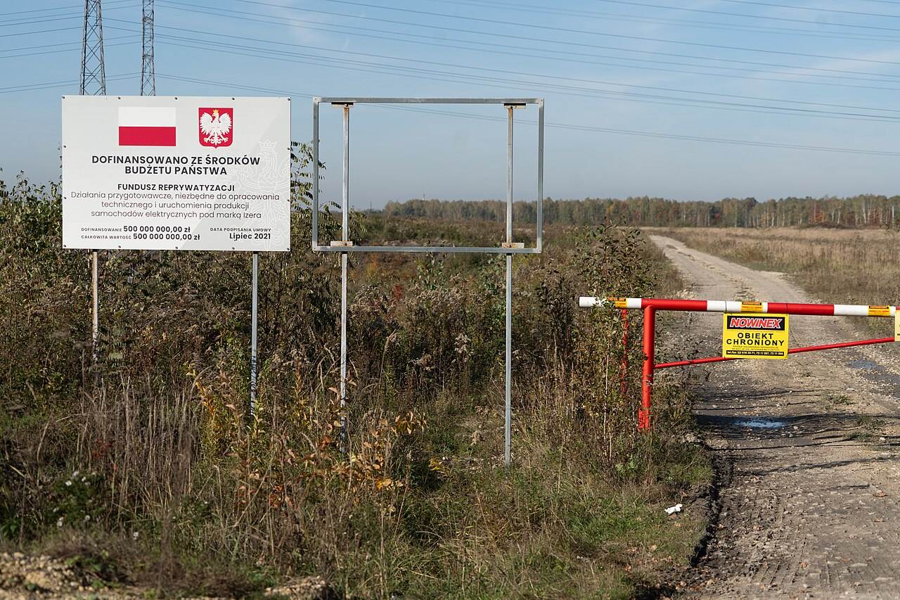 Teren pod budowę fabryki samochodów elektrycznych w Jaworznie — ogrodzony plac z tablicą o dofinansowaniu ze środków budżetu państwa
