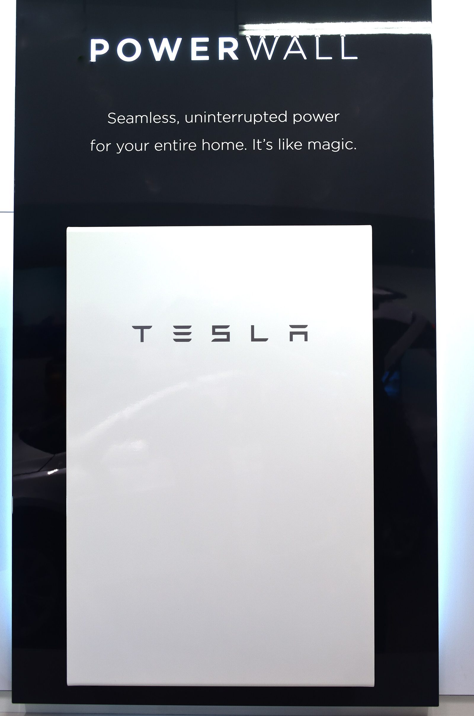 Domowy magazyn energii prezentowany na ekspozycji producenta — biały moduł z logo Tesla