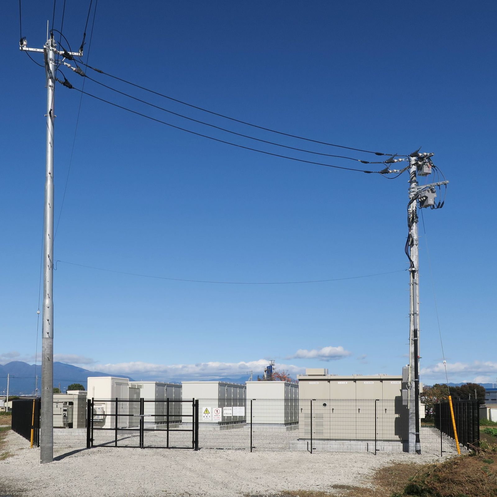 Kontenery bateryjnego magazynu energii za ogrodzeniem, przyłączone do sieci energetycznej