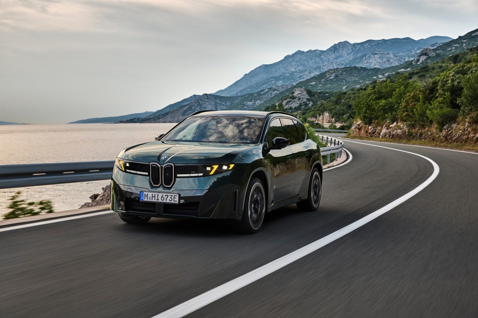 BMW iX3 M60 xDrive, ciemnozielony elektryczny SUV Neue Klasse, podczas jazdy nadmorską drogą