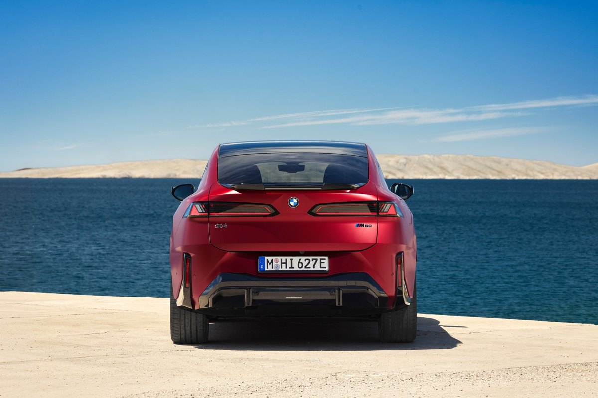 BMW iX4 M60 xDrive, elektryczne SUV coupé, widok z tyłu nad brzegiem morza