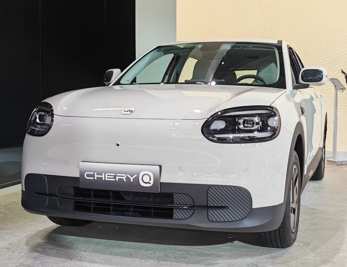 Biały Chery Q, mały elektryk, widok z przodu na tle ściany salonu
