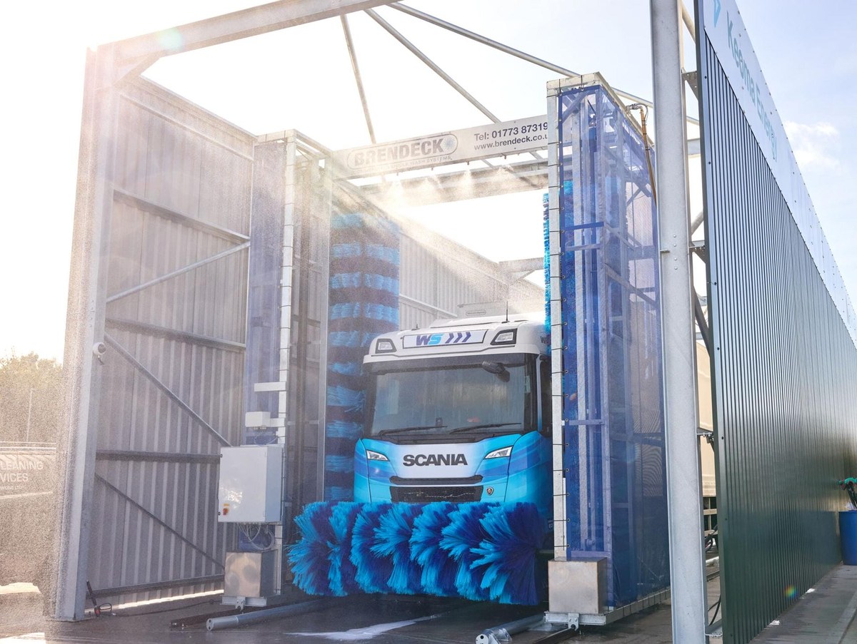 Niebieska elektryczna Scania przejeżdża przez myjnię samochodową na terenie hubu Electroway