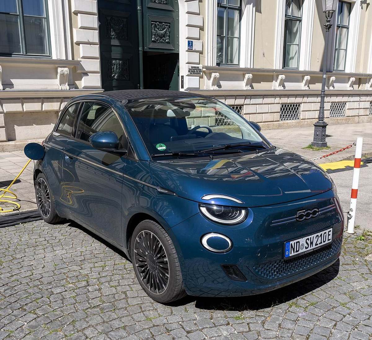 Niebieski Fiat 500e z kablem ładowania na ulicy w Monachium