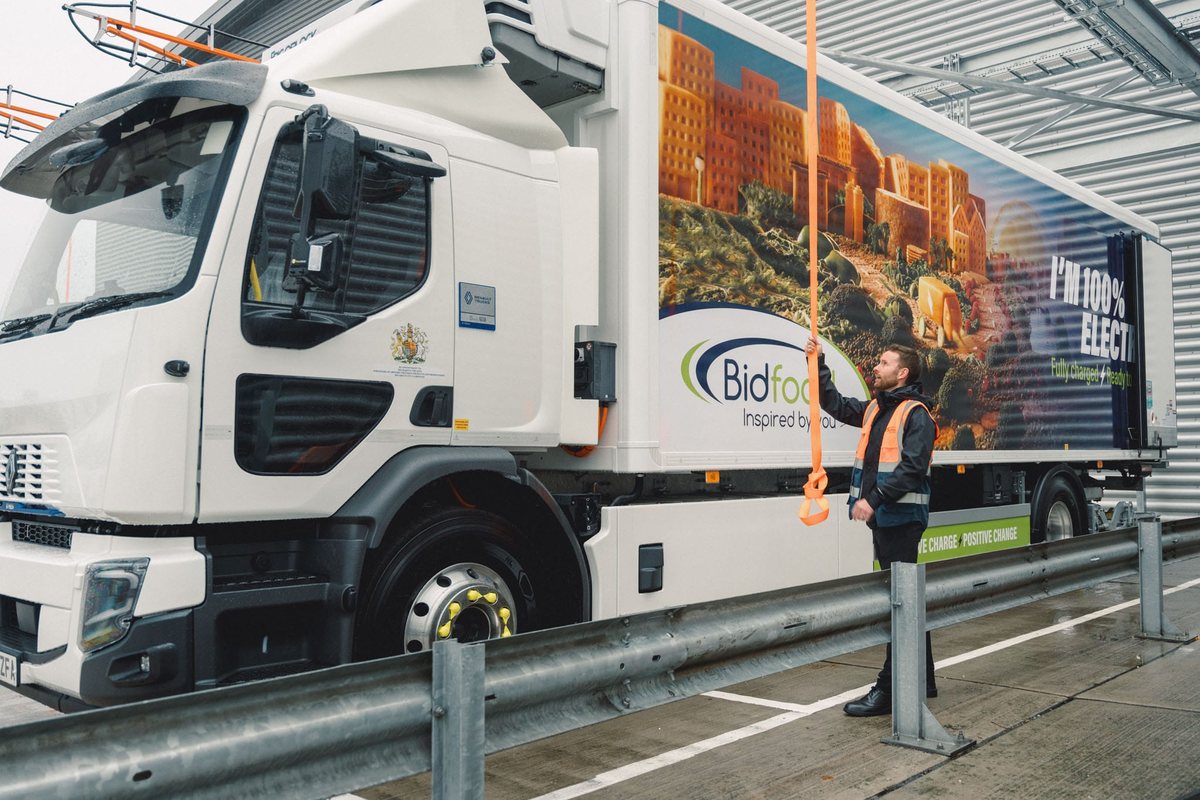 Kierowca podłącza wtyczkę z ramienia ładowania do elektrycznej ciężarówki Renault Trucks w zajezdni Bidfood