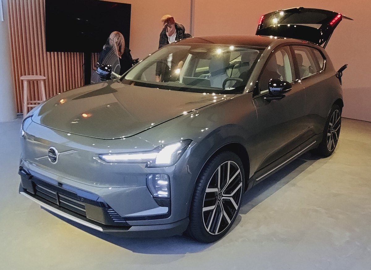 Volvo EX60 w szarym lakierze na wystawie w pomieszczeniu, z otwartą klapą bagażnika